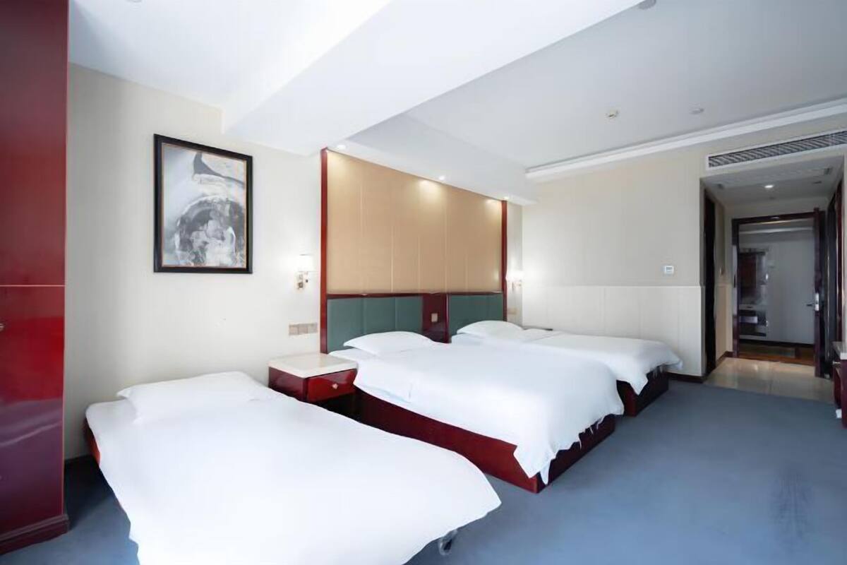 A hotel room with three beds, a large mirror, and a red wardrobe.