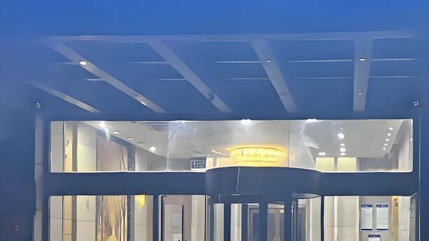 A modern building entrance with a glass facade, a revolving door, and a circular light fixture above the door. - Memory Hotel (Zhenjiang)