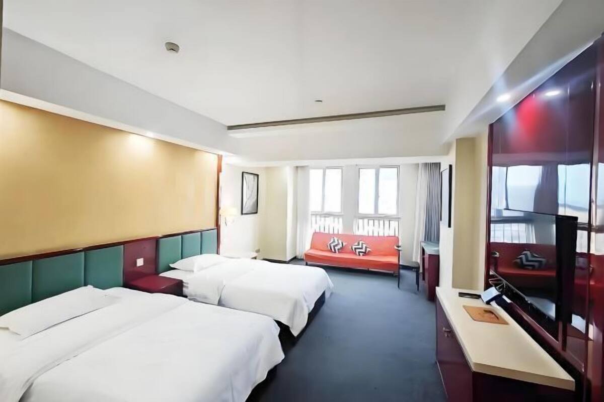A hotel room with two beds, a sofa, a TV, and a window with curtains.