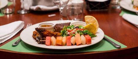 Un plato de comida con brochetas, ensalada y un gajo de limón sobre una mesa.