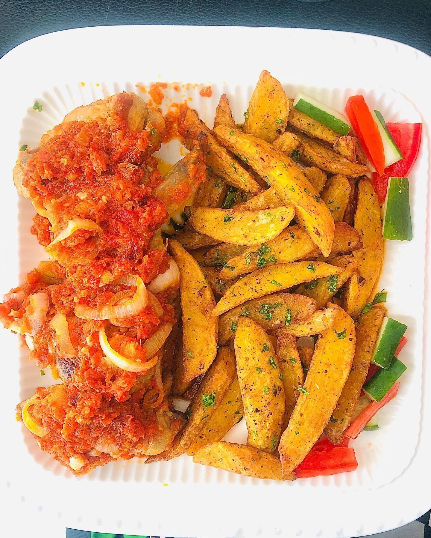 A plate with fried fish, seasoned fries, and sliced vegetables.
