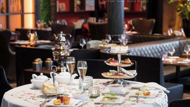 Un comedor con mesas redondas dispuestas para una comida, con un expositor escalonado de postres, servicio de té y copas de vino.