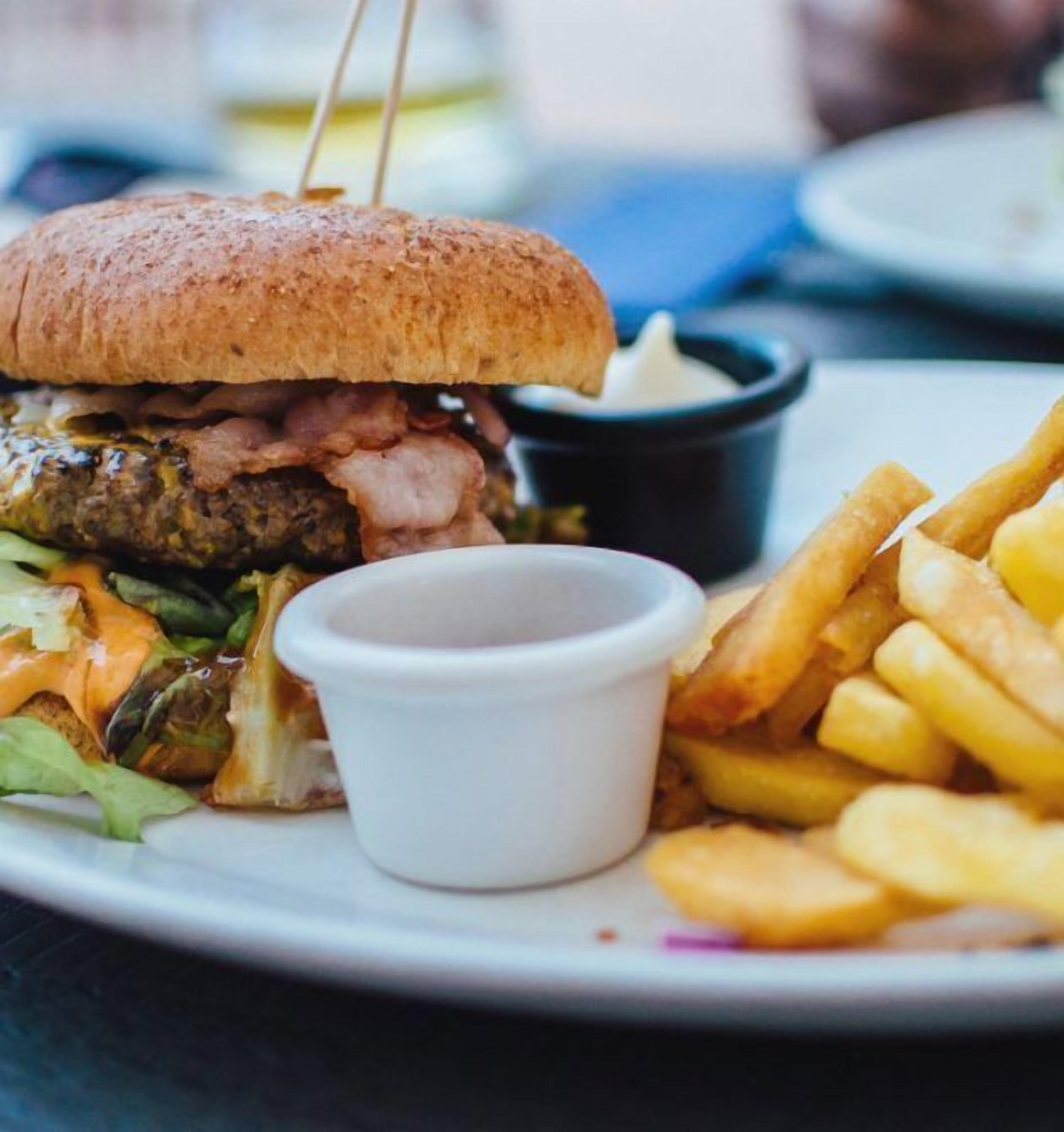 A plate with a burger, fries, and a small cup of sauce.