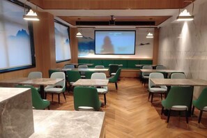 A conference room with a large screen, green chairs, and tables arranged for meetings. - Outing Boutique Hotel Yiwu International Trade City (Yiwu)
