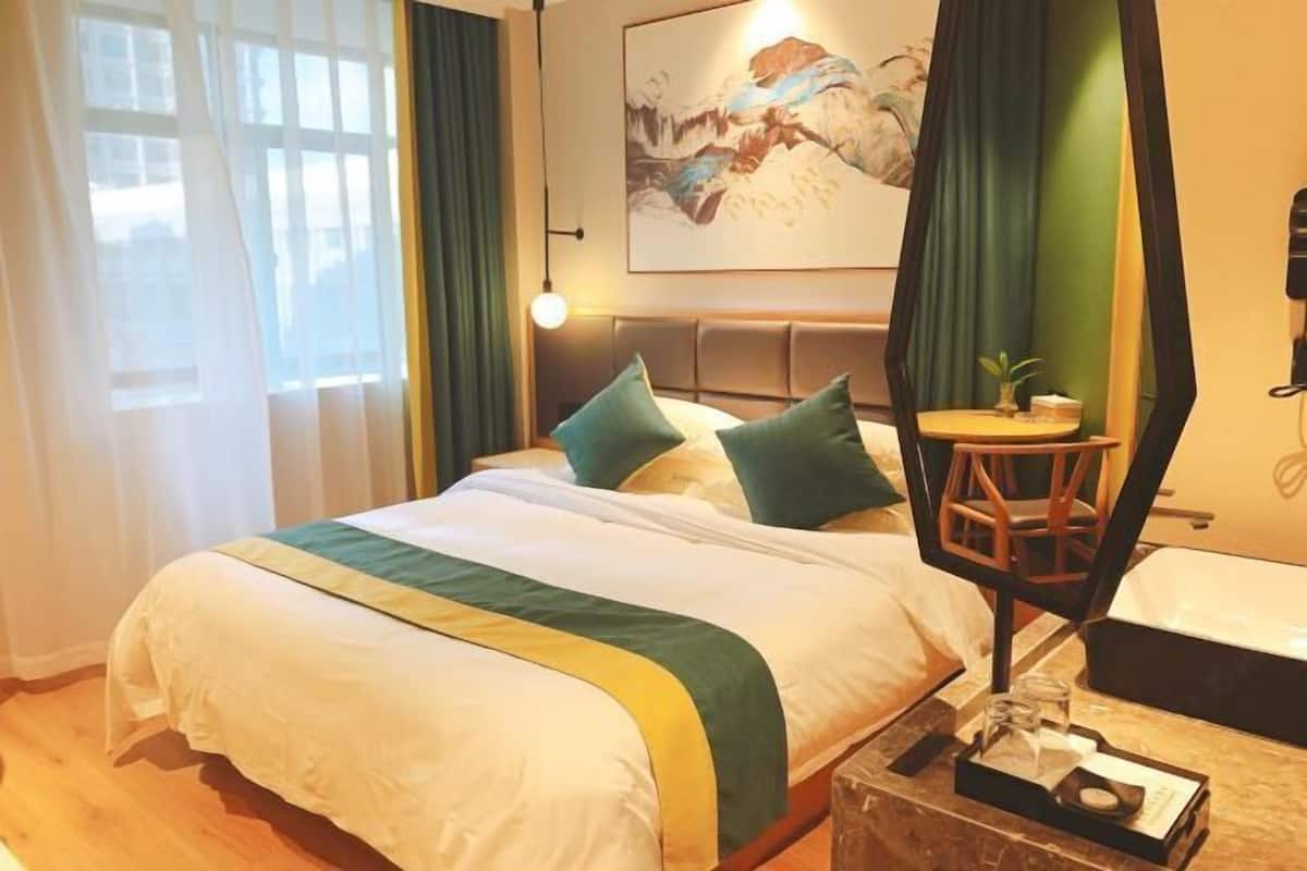 Et hotelværelse med en seng, et sengebord med lampe, et billede på væggen og udsigt til det fri.