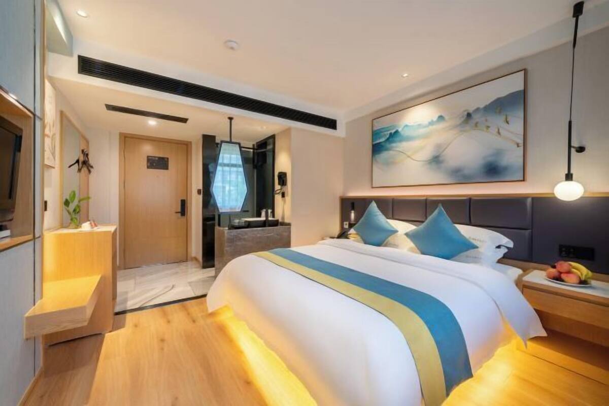 Et moderne hotelværelse med en stor seng, et skrivebord, et spejl og et billede på væggen.