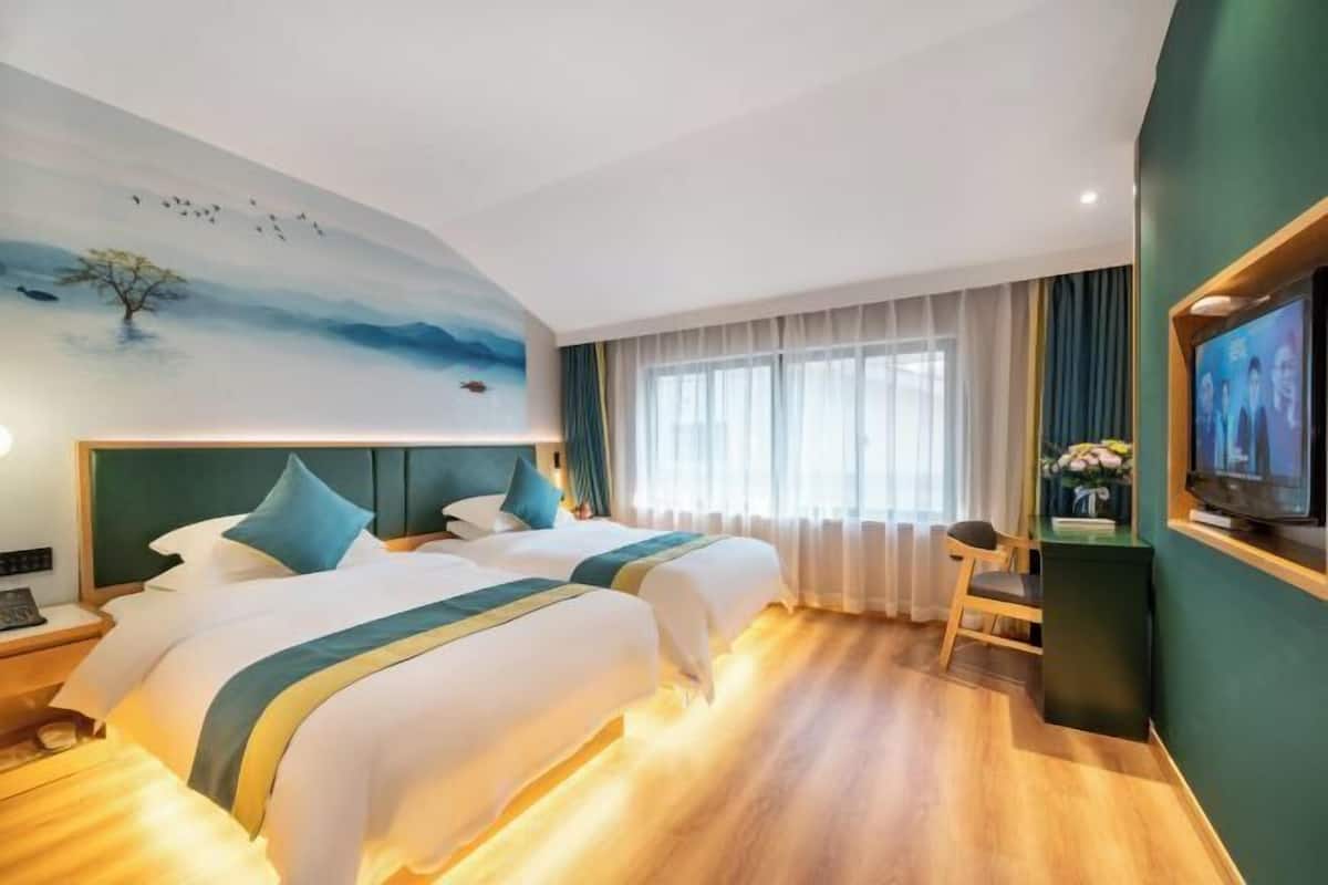 Et hotelværelse med to senge, et skrivebord, et fjernsyn og et muralmaleri på væggen.
