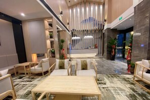 A modern hotel lobby with a reception desk, seating area, and a staircase leading to the upper floor.
