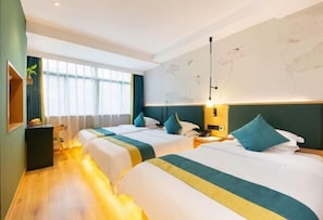 Quarto de hotel com duas camas, uma janela grande, uma parede com arte floral e uma mesa de cabeceira com abajur.