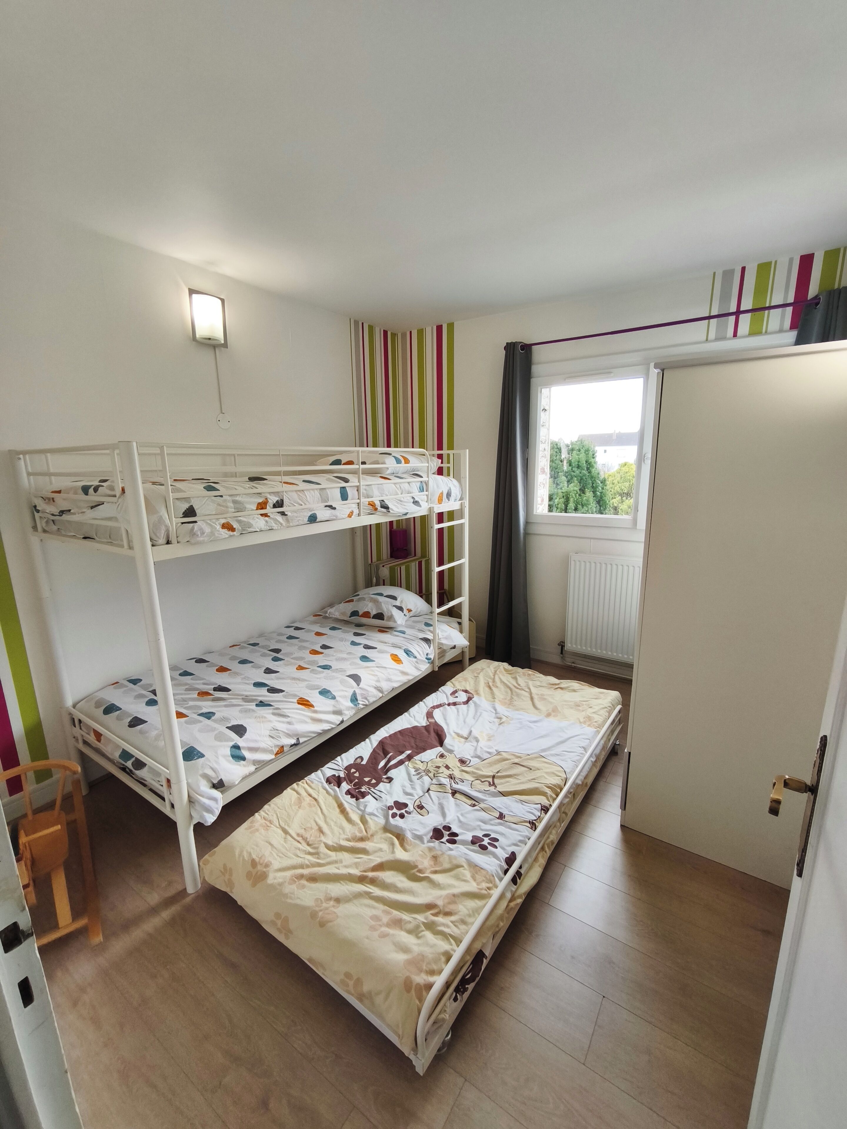Een slaapkamer met stapelbed, raam, verwarming en deur.