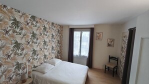 Un dormitorio con cama, una silla, un ventanal y una pared con diseño de hojas.