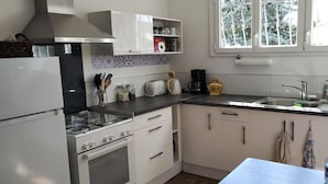 Una cocina moderna con armarios blancos, horno empotrado, estufa, lavaplatos y ventana con vista a árboles.