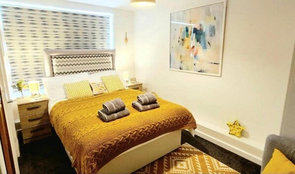 A neatly arranged bedroom with a bed, bedside tables, a bedside lamp, a window with blinds, and a wall-mounted abstract painting. - 2bdr- sea Breeze - Family Friendly- Parking-int (Bournemouth)