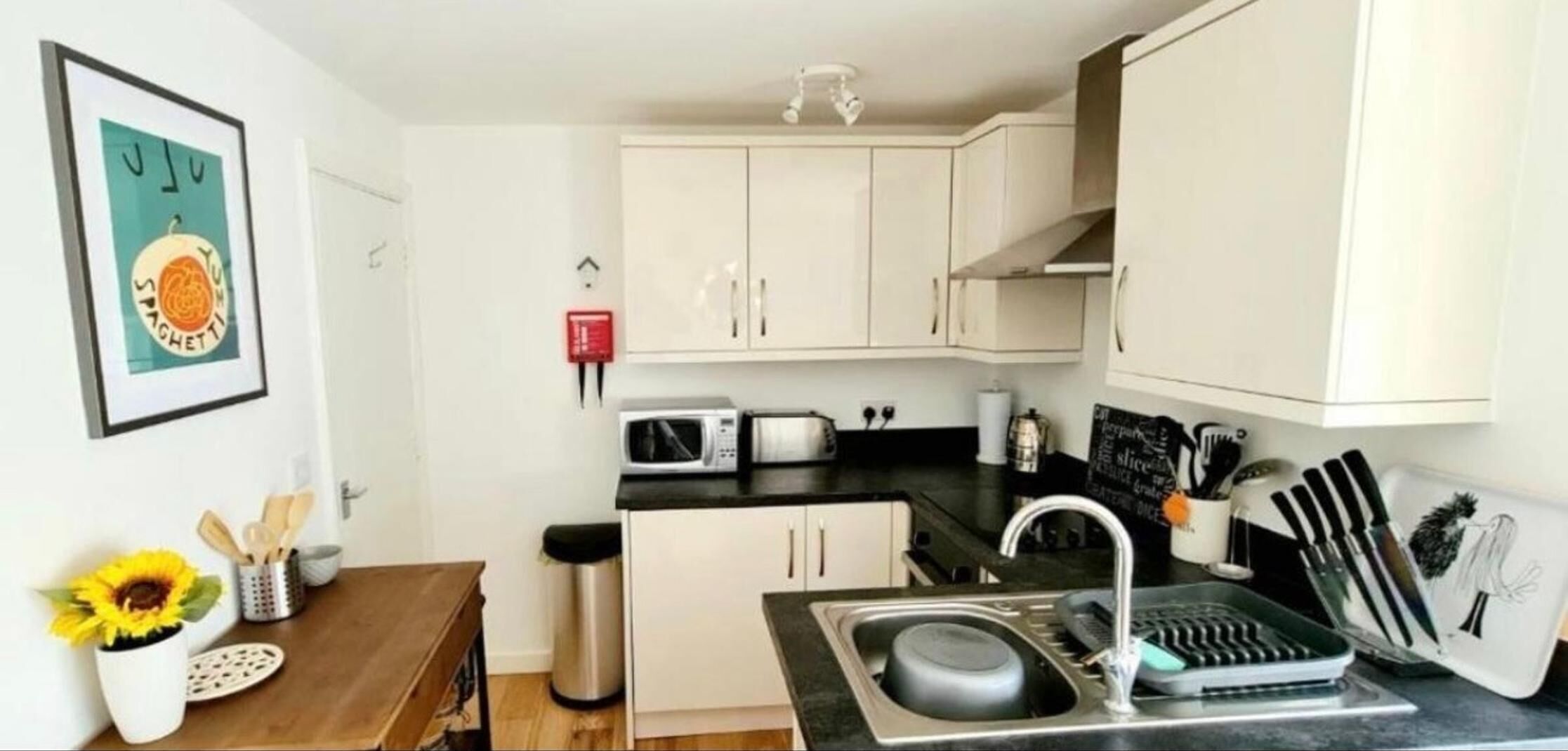 A compact kitchen with white cabinets, a sink, a microwave, a toaster, and a small dining table with a sunflower decoration.
