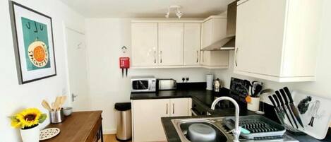 A compact kitchen with white cabinets, a sink, a microwave, a toaster, and a small dining table with a sunflower decoration.