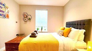 Une chambre à coucher avec un lit, une fenêtre, une étagère hexagonale fixée au mur et une petite table avec une lampe.