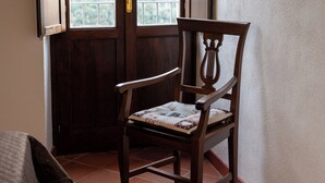 Habitación de esquina con una silla de madera, una ventana que ofrece vistas a una montaña y suelo de baldosas.