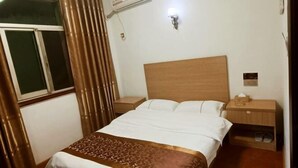 Hotellihuone, jossa on puinen sängynpääty, suuri sänky kuviollisella peitteellä, yöpöytä lampun kanssa ja ikkuna, jossa on verhot.