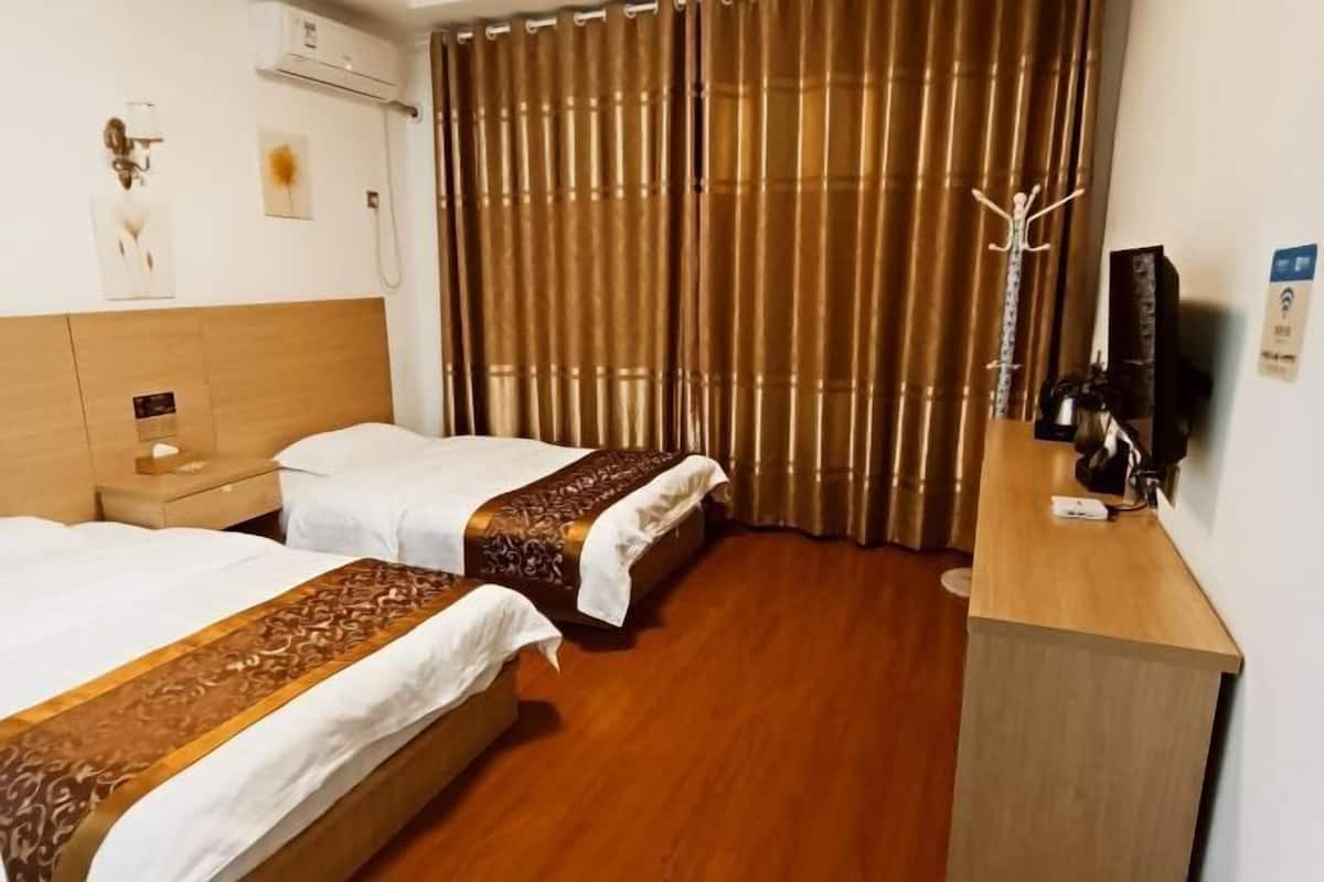 A hotel room with two beds, a wooden headboard, a desk with a chair, a coat rack, and a television.