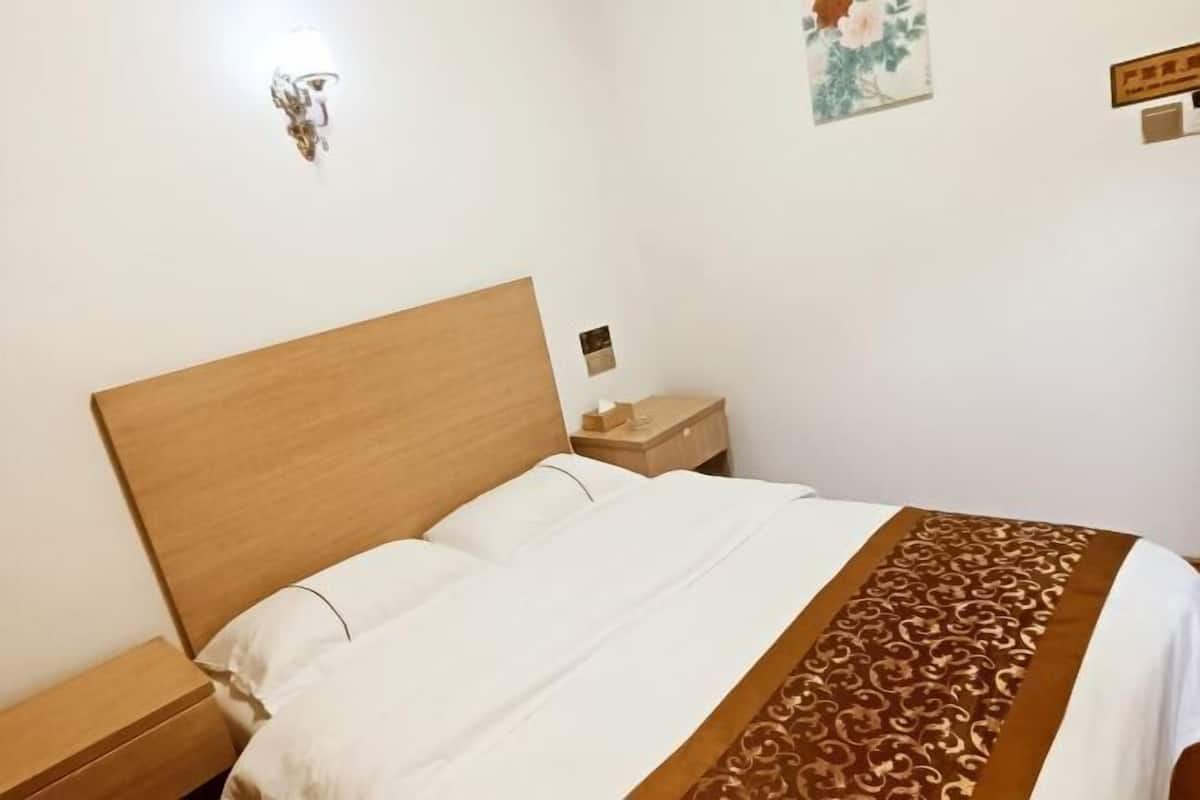 A neatly made bed with a wooden headboard, a bedside table with a lamp, and a wall-mounted light fixture.