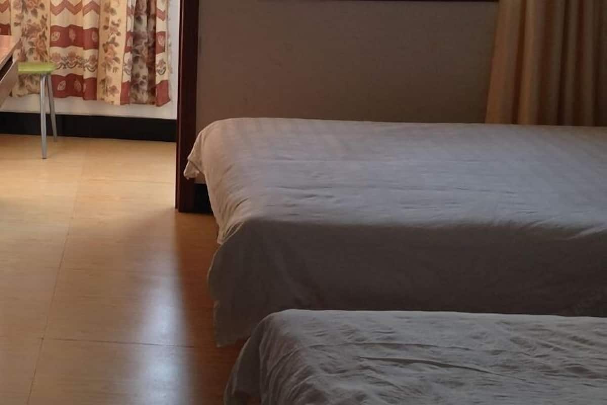 A bedroom with two beds, a wooden floor, a chair, and a curtain with a floral pattern.