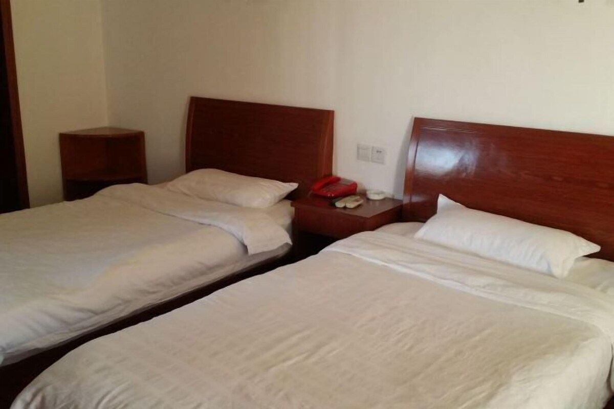 Ein Hotelzimmer mit zwei Einzelbetten, Holz-Kopfteilen, einem Nachttisch mit Telefon und einer Steckdose.
