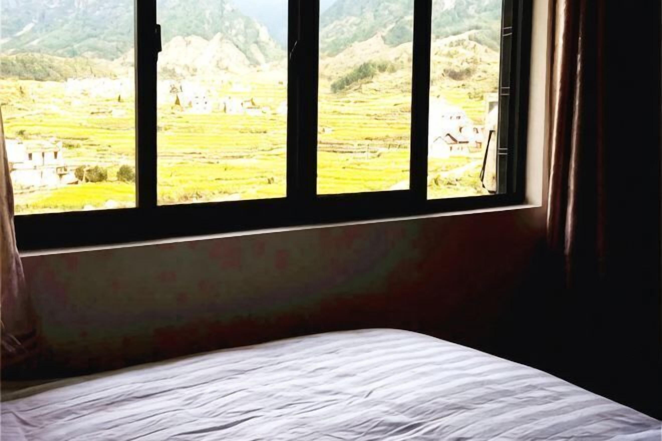 A room with a bed, a window, and a view of a landscape.