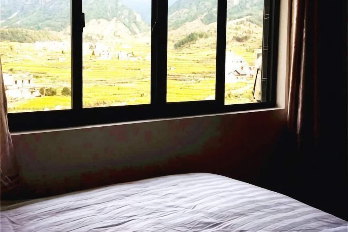 A room with a bed, a window, and a view of a landscape.