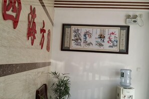 Una pared con caracteres chinos, una obra de arte enmarcada y un dispensador de agua.