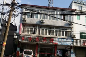 Un edificio de varios pisos con una planta baja comercial, que presenta un escaparate con señalización y un vehículo estacionado.