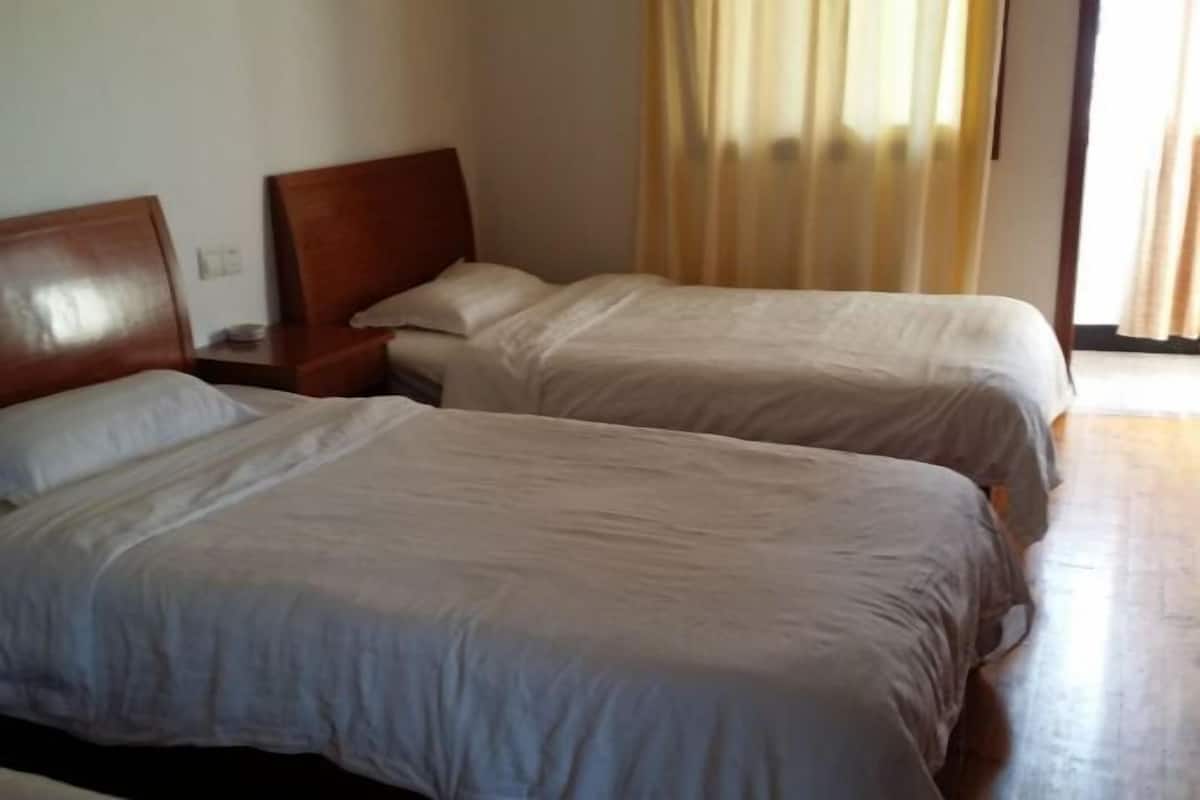 A hotel room with two beds, wooden headboards, a nightstand, and a window with curtains.