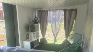 A hot tub in a room with a view of a grassy area, a green chair, and a shelf with decorative items. - Gite Cosy Dans un Cadre Verdoyant Entre Méditerranée et Gorges du Verdon (Flassans-sur-Issole)