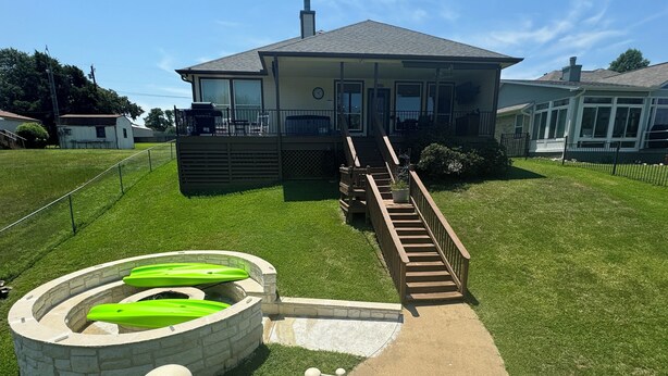 A house with a covered porch, a stone well, and a wooden staircase leading to a deck.