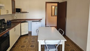 A compact kitchen with a microwave, stove, and small refrigerator. There's a dining table with chairs and a white cabinet.