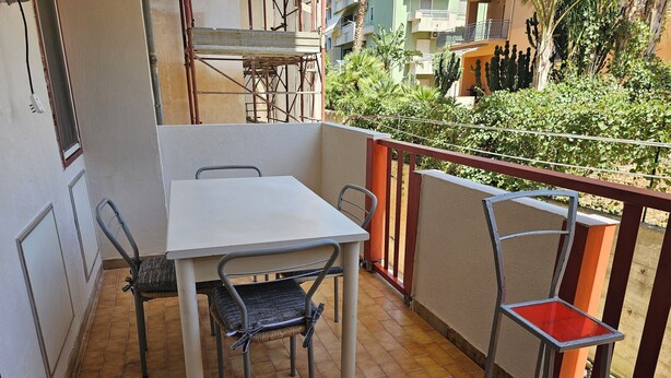 A balcony with a white table and two chairs, a red stool, and a metal chair with a red seat.