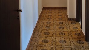 A hallway with patterned floor tiles, a mirror on the wall, and a door on the left.