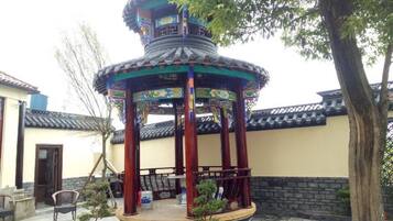 Un pabellón tradicional con techo de tejas, rodeado por un patio empedrado con un árbol y un columpio.