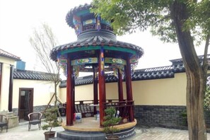 A traditional pavilion with a tiled roof, surrounded by a paved courtyard with a tree and a swing set. - Yiyi Hotel (Dujiangyan)