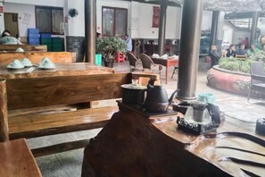 A traditional wooden dining area with benches and tables, a central pillar, and a small garden area with plants.