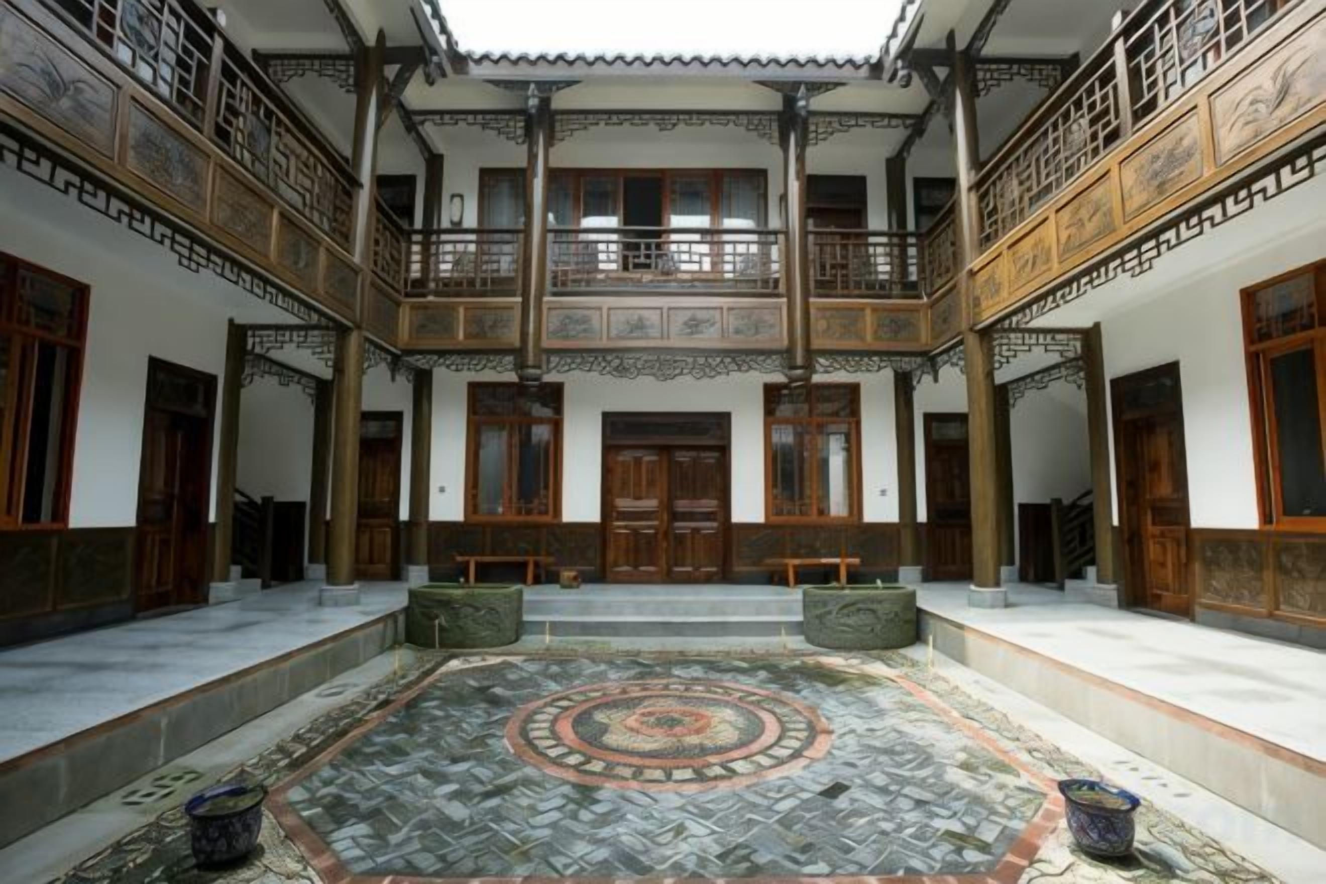 Um pátio tradicional com piso de azulejos no centro, portas de madeira e uma varanda com grades detalhadas.