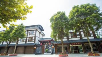 A traditional building with a tiled roof, a central entrance with a decorative arch, and a courtyard with trees and potted plants.