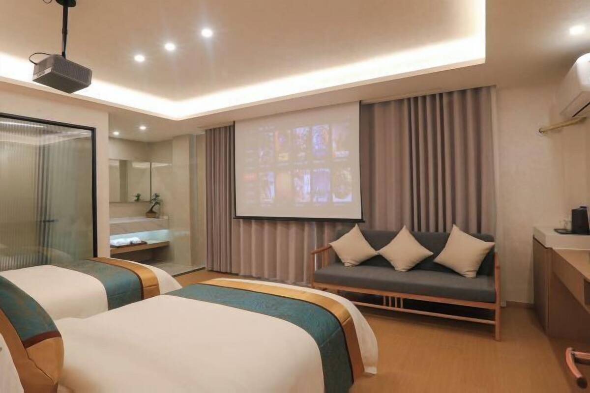 Une chambre d’hôtel avec deux lits, un canapé, un écran de projection et un bureau.