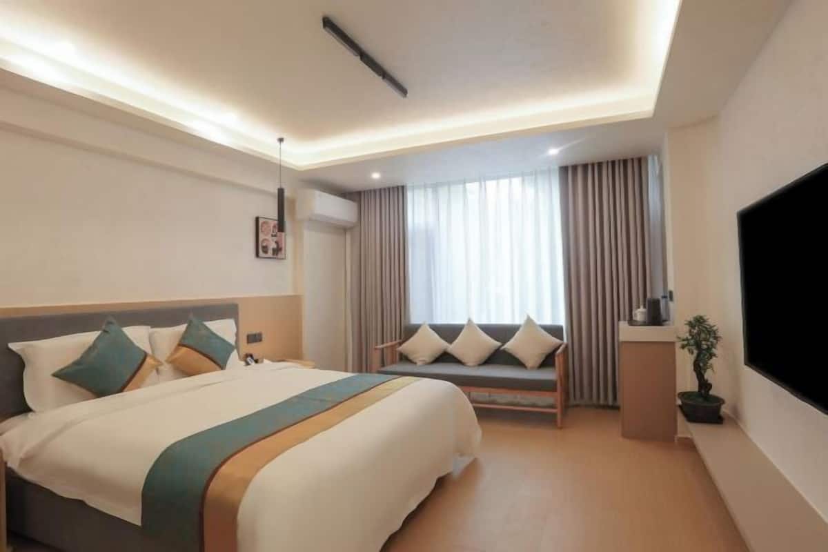 Une chambre d’hôtel avec un lit, un canapé, une télévision et une fenêtre avec des rideaux.