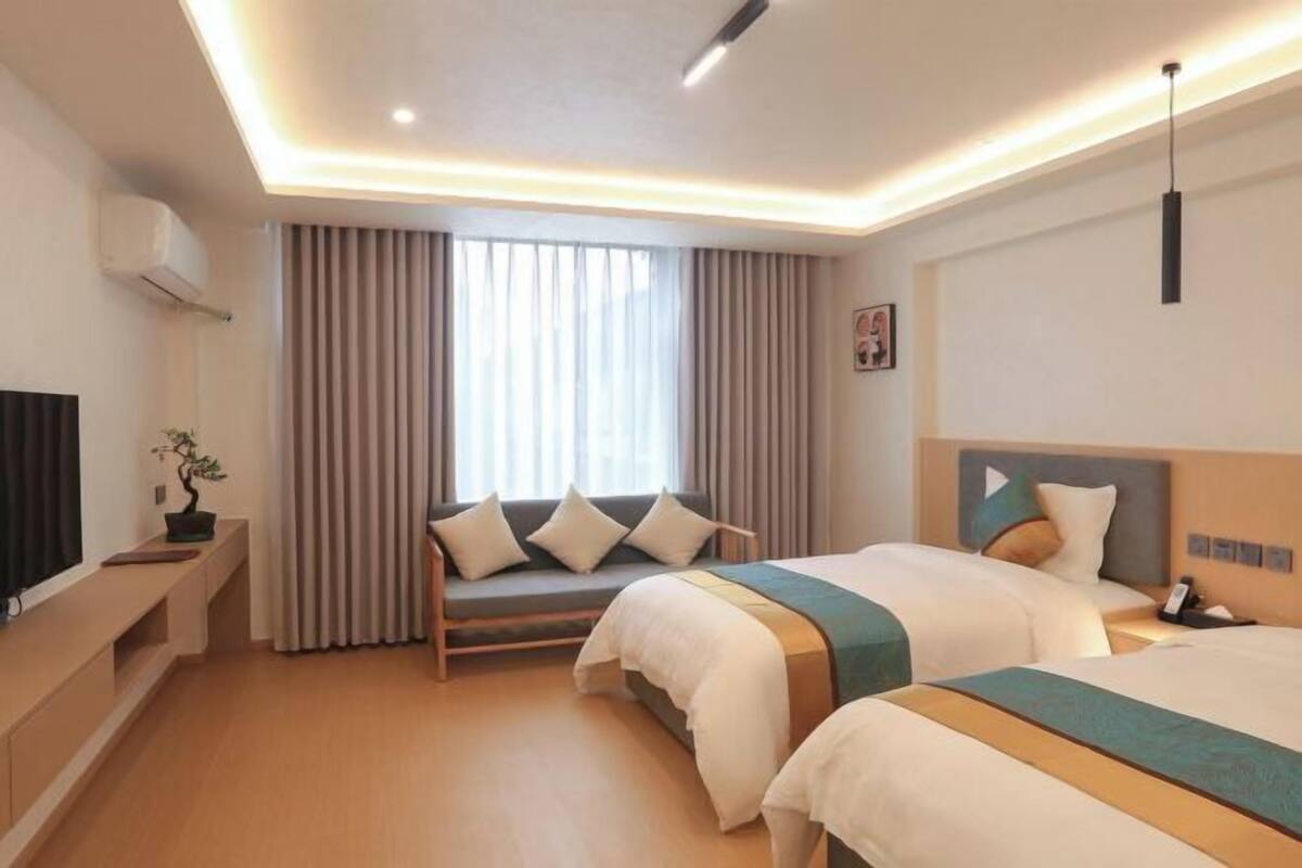 Une chambre d’hôtel avec deux lits, un canapé, une télévision et une grande fenêtre avec des rideaux.