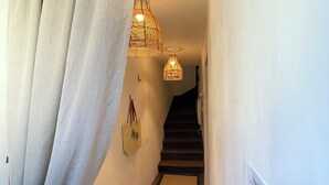 Un pasillo con una escalera, un lámpara colgante y un bolso sujeto a la pared.