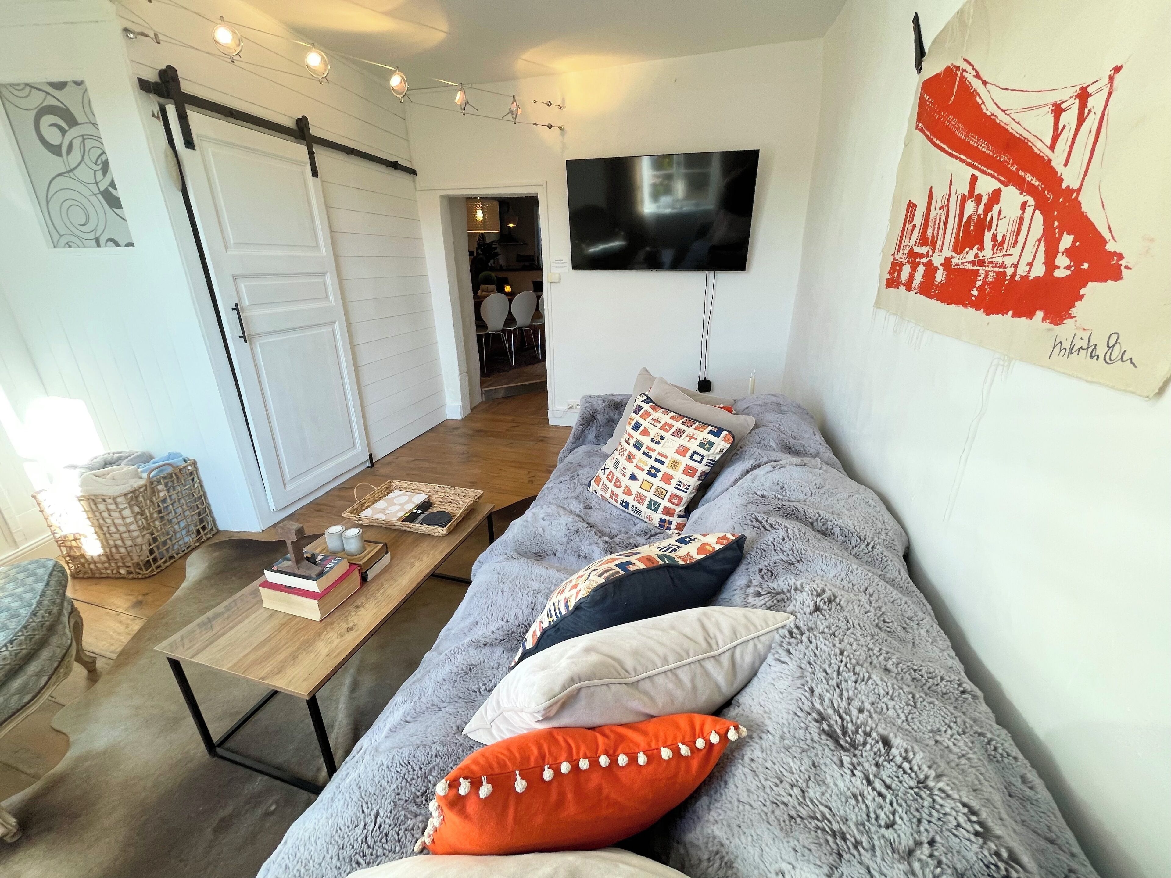 Un salon chaleureux avec un canapé gris, une table basse en bois et un téléviseur fixé au mur.