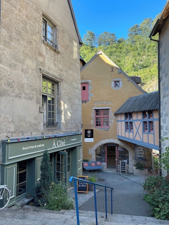 A narrow street with buildings featuring traditional architecture, including a café with outdoor seating and a sign for 'Le Café Canine'.