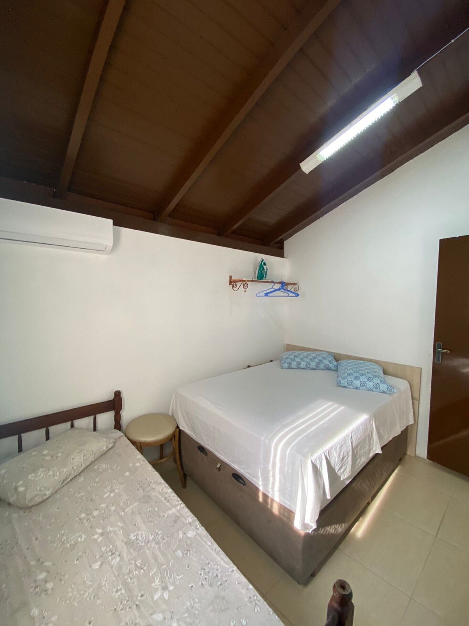 Un dormitorio con una cama, una cama individual, una silla, un estante con una plancha y una puerta.