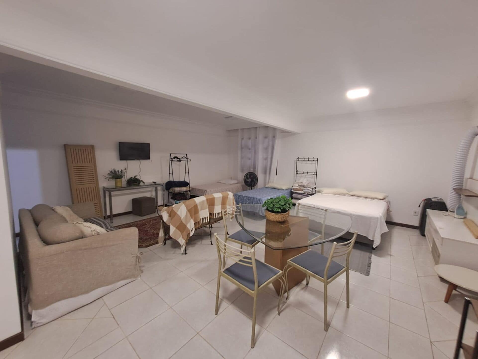 Un espacio habitable compacto con sofá, mesa de comedor con sillas, cama, escritorio pequeño con silla y televisión montada en la pared.