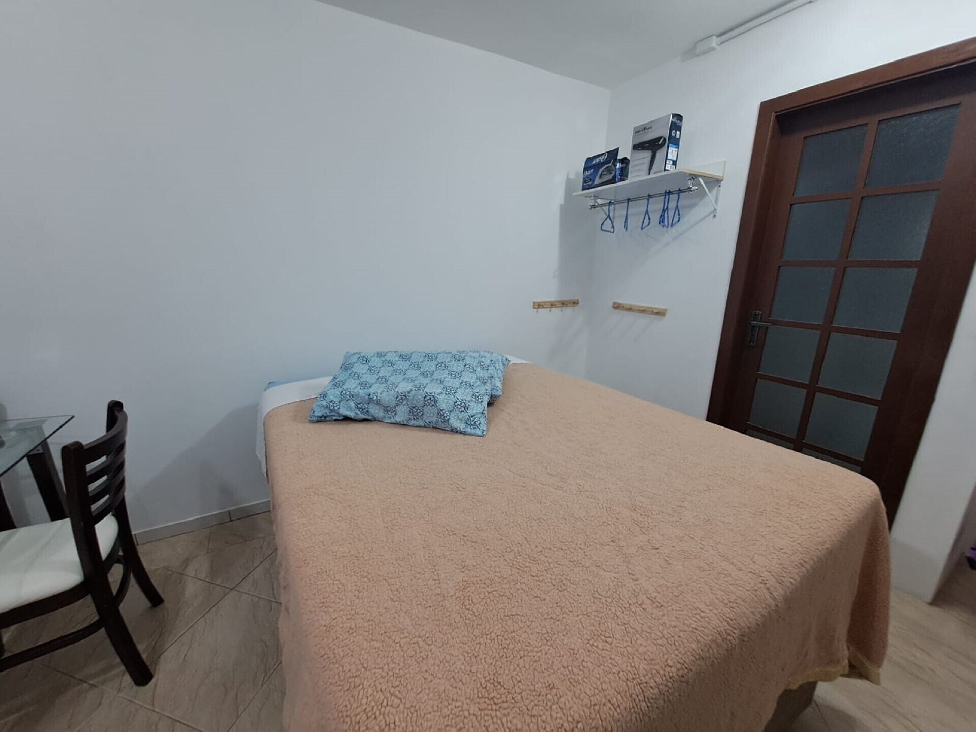 A small, tidy room with a bed, a chair, a shelf with items, and a door.